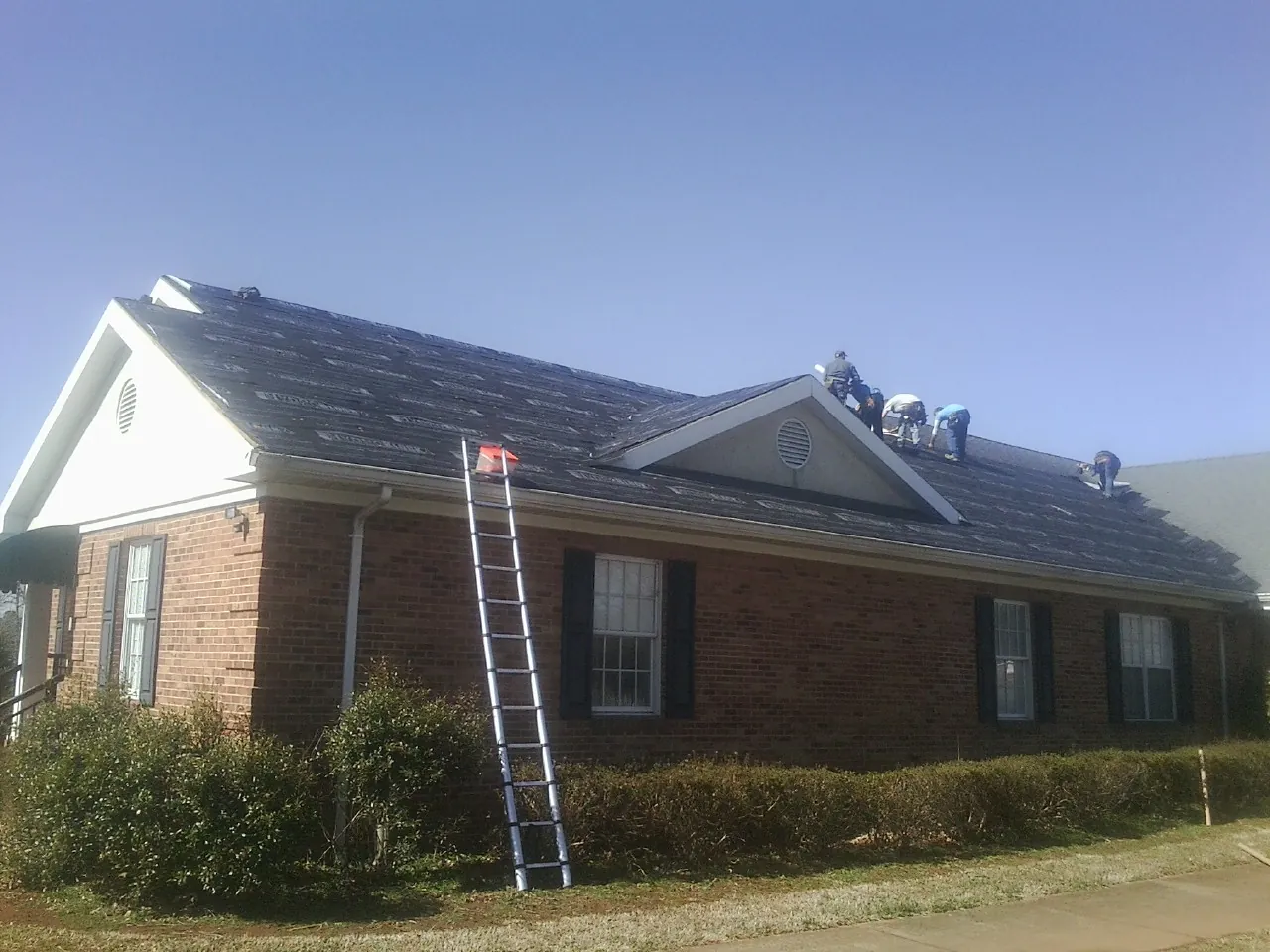 Crew tearing shingles off a brick ranch roof with a ladder set — Metal Roof Repair work by our crew in Woodward