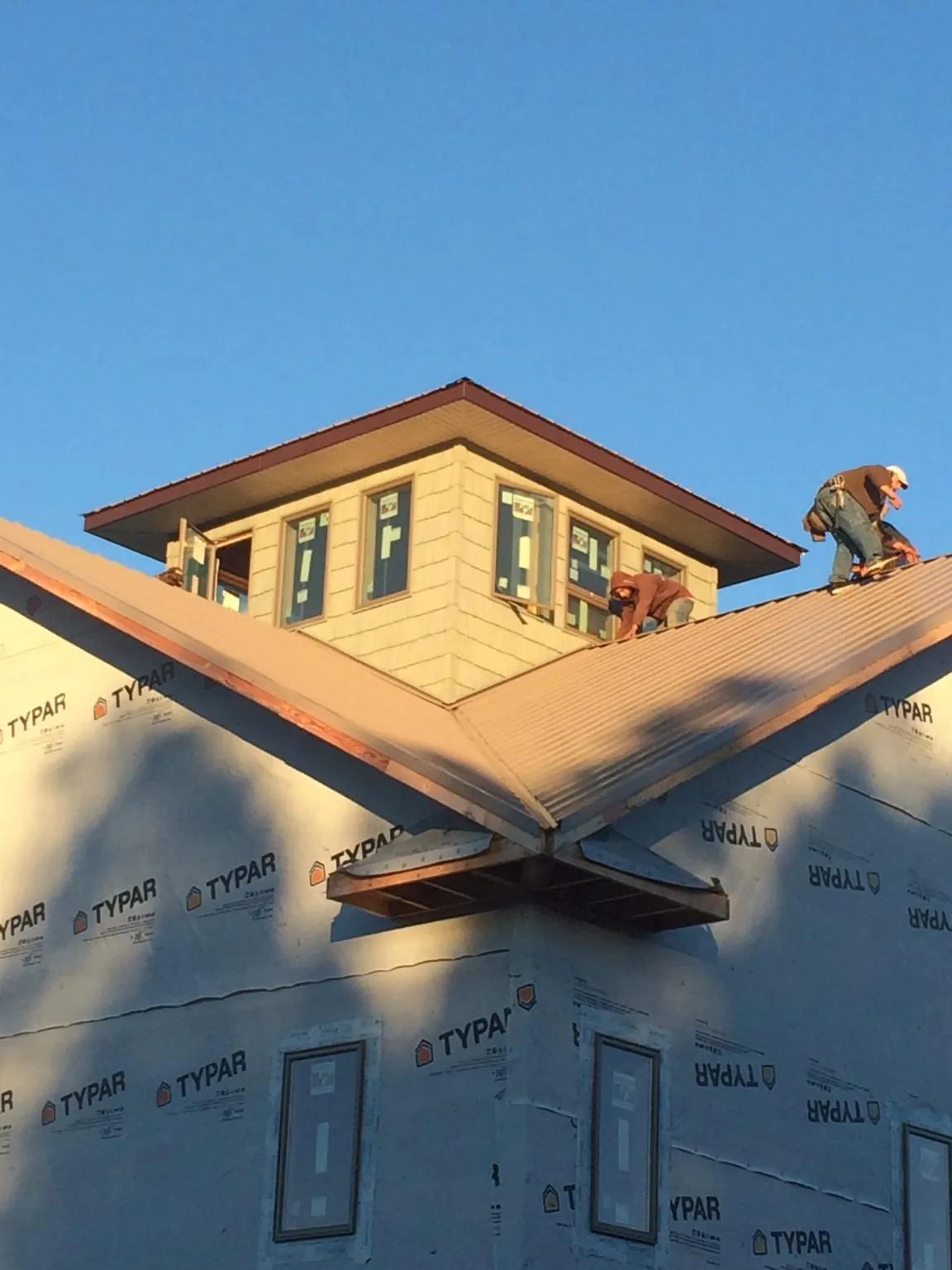 Roofers working around a rooftop cupola on a new metal roof at sunset — Roof Waterproofing in Woodward by Roofing Brothers